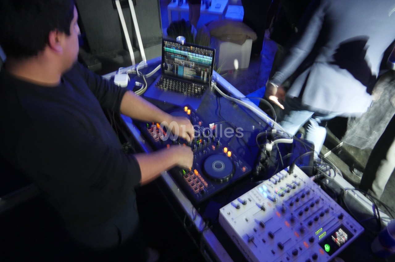 Un DJ mixe de la musique sur une console avec un ordinateur portable dans un environnement éclairé en bleu.