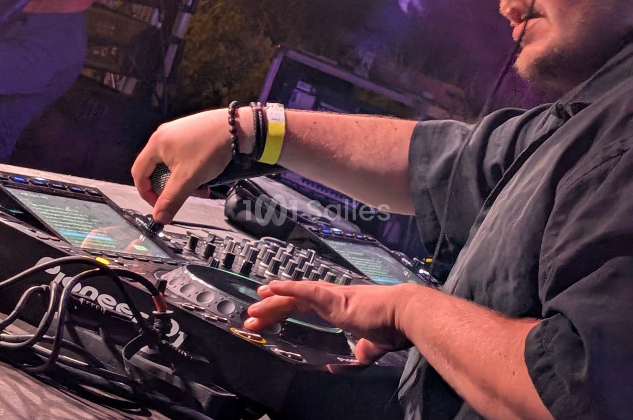 Un DJ mixe de la musique sur une table de mixage lors d'une performance en extérieur.