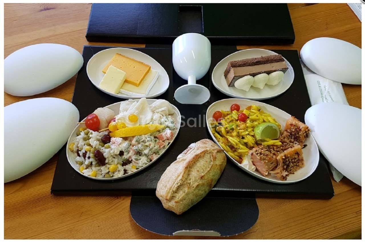 Plateau-repas avec pain, fromage, salade composée, poisson, desserts variés et verre sur une table en bois.
