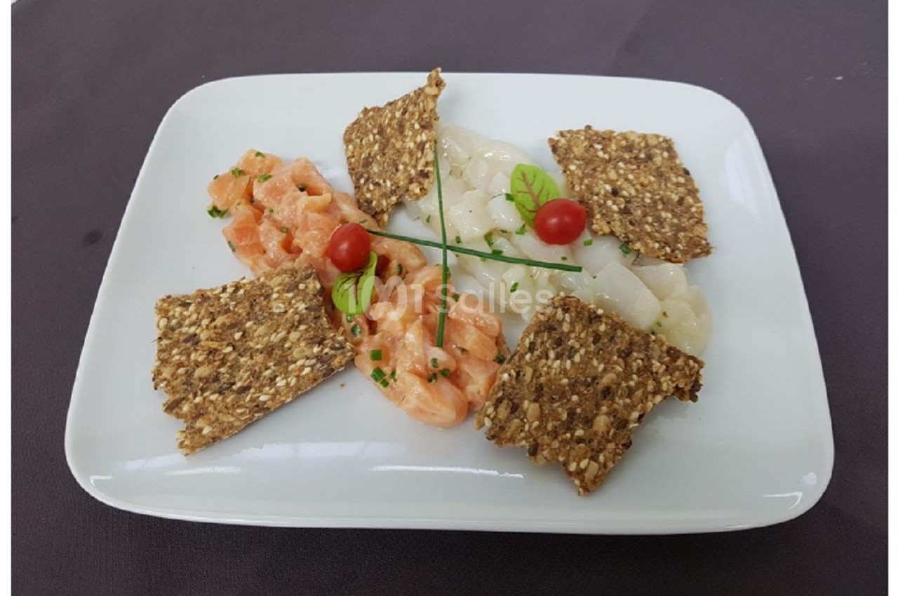 Assiette composée de tartare de saumon, de carpaccio de Saint-Jacques, de crackers aux graines et de décorations végétales.