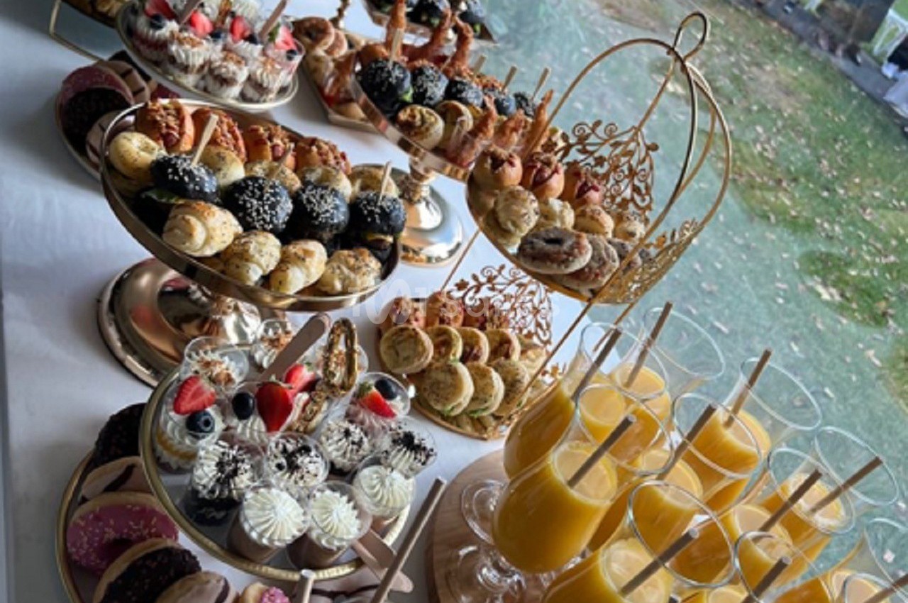 Plateaux de pâtisseries variées et verres de jus d'orange disposés sur une table près d'une fenêtre.