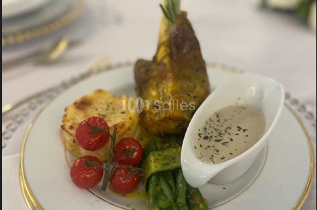 Assiette garnie d'un jarret d'agneau, gratin dauphinois, haricots verts, tomates cerises et sauce servie à part.