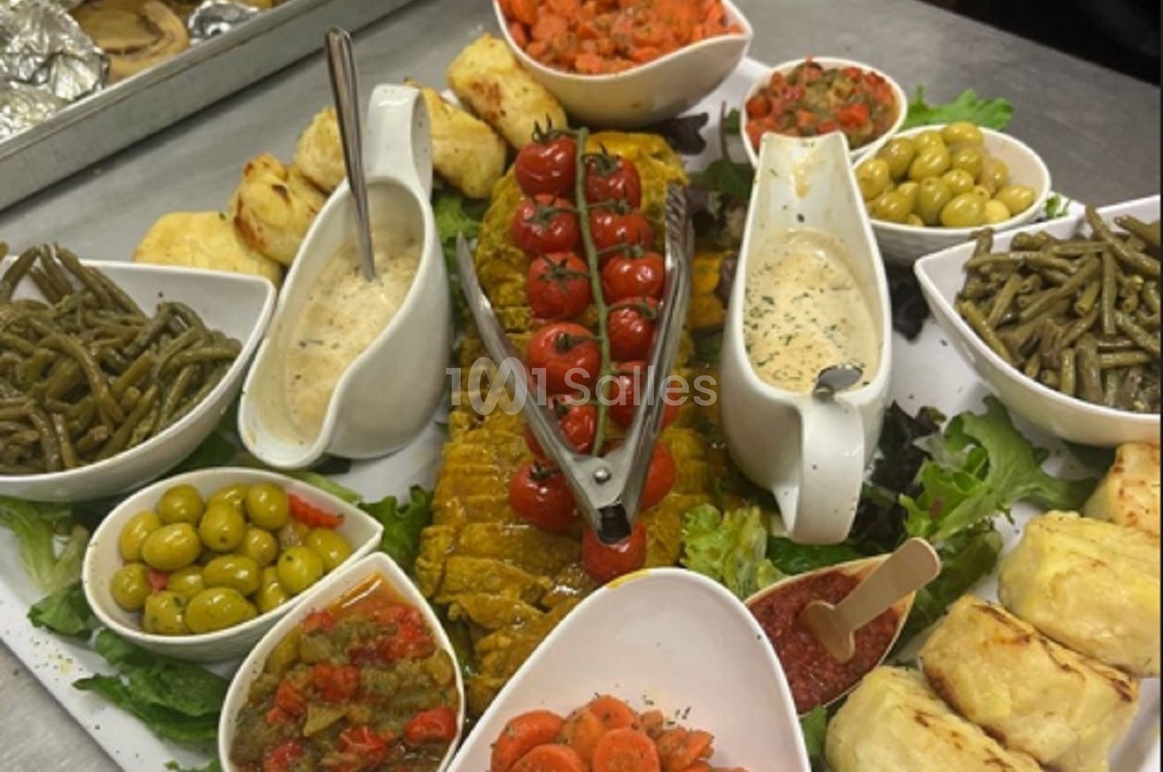 Plateau de service avec légumes variés, sauces, tomates cerises grillées et accompagnements disposés sur un lit de salade.