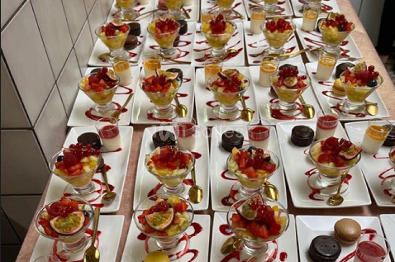 Plateaux de desserts variés avec verrines de fruits, macarons, sauces et décorations colorées sur des assiettes blanches.