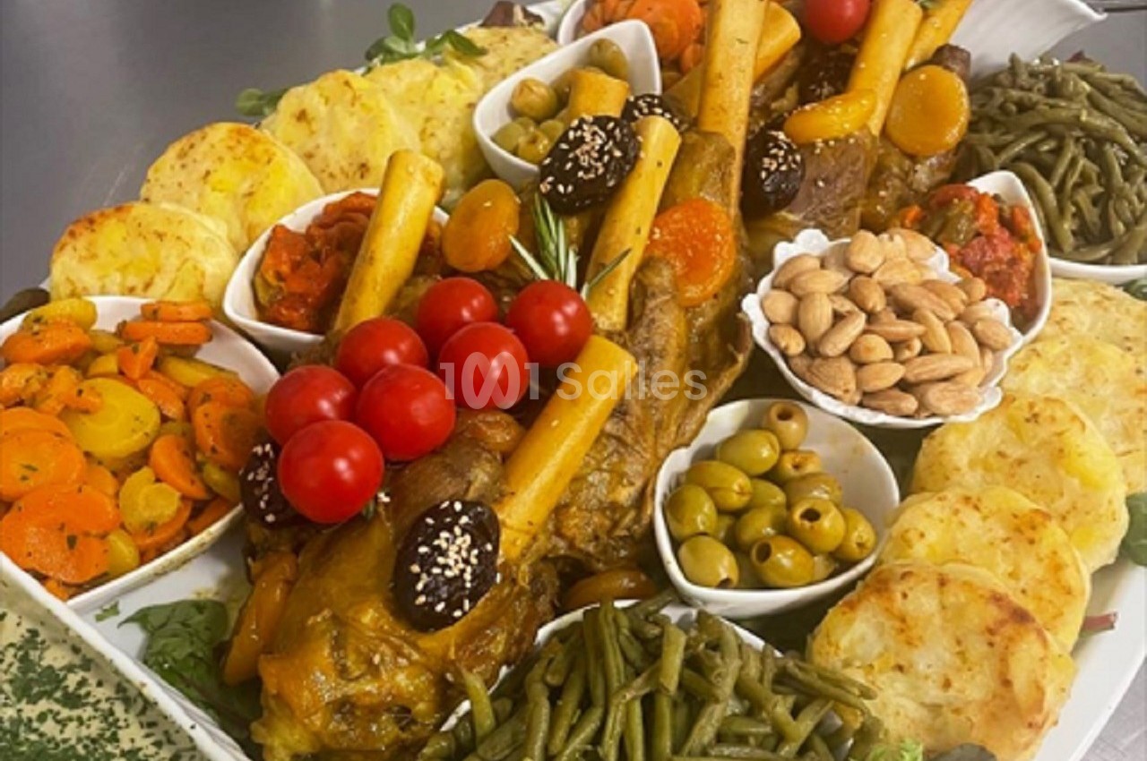 Plateau garni de jarrets d'agneau, légumes variés, olives, amandes et accompagnements disposés harmonieusement.
