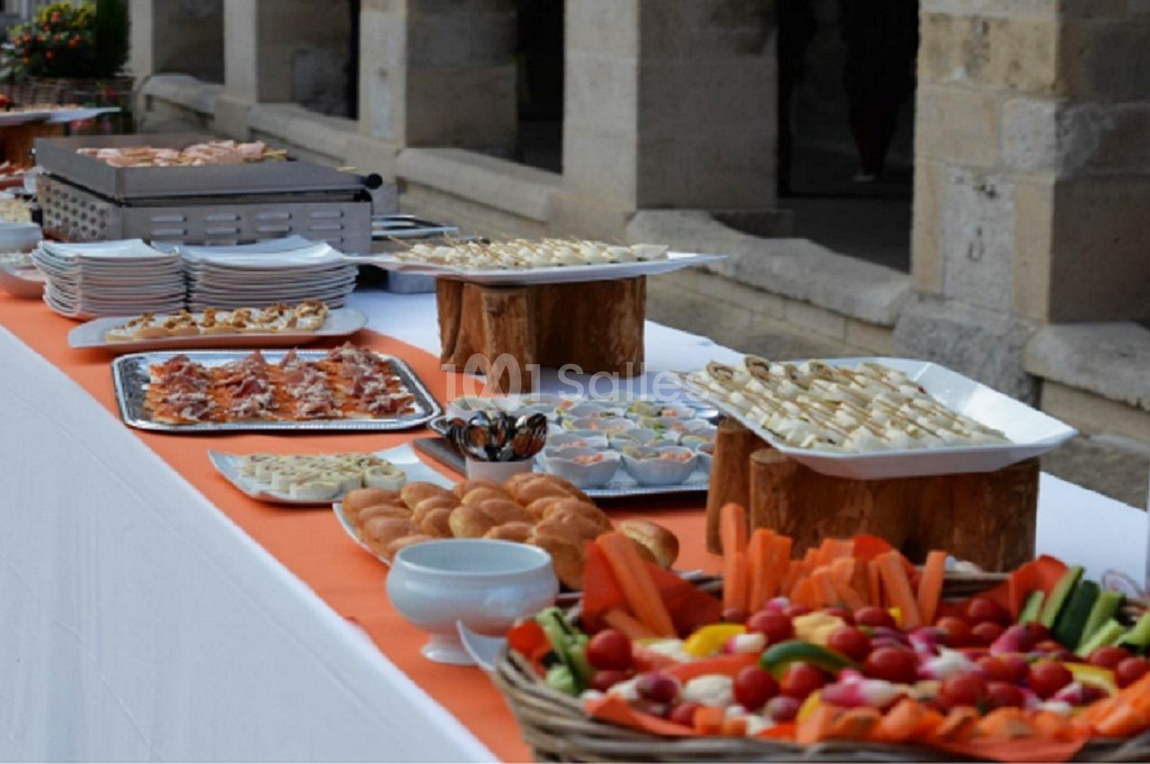 Buffet extérieur avec plateaux de légumes, viennoiseries, amuse-bouches et plats variés sur une table blanche.