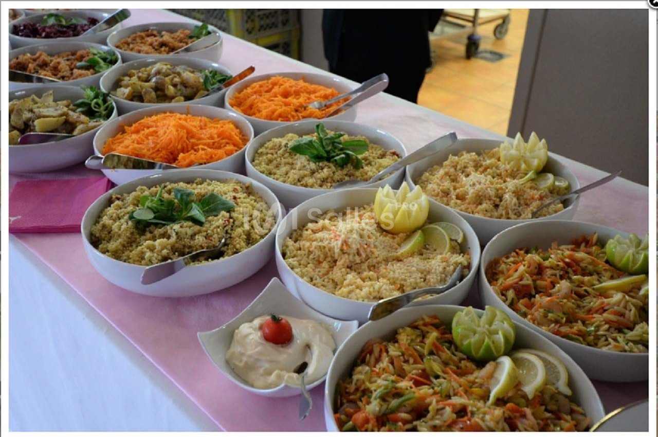 Buffet de salades variées avec carottes râpées, taboulé, légumes, et sauce, présenté dans des bols sur une nappe rose.