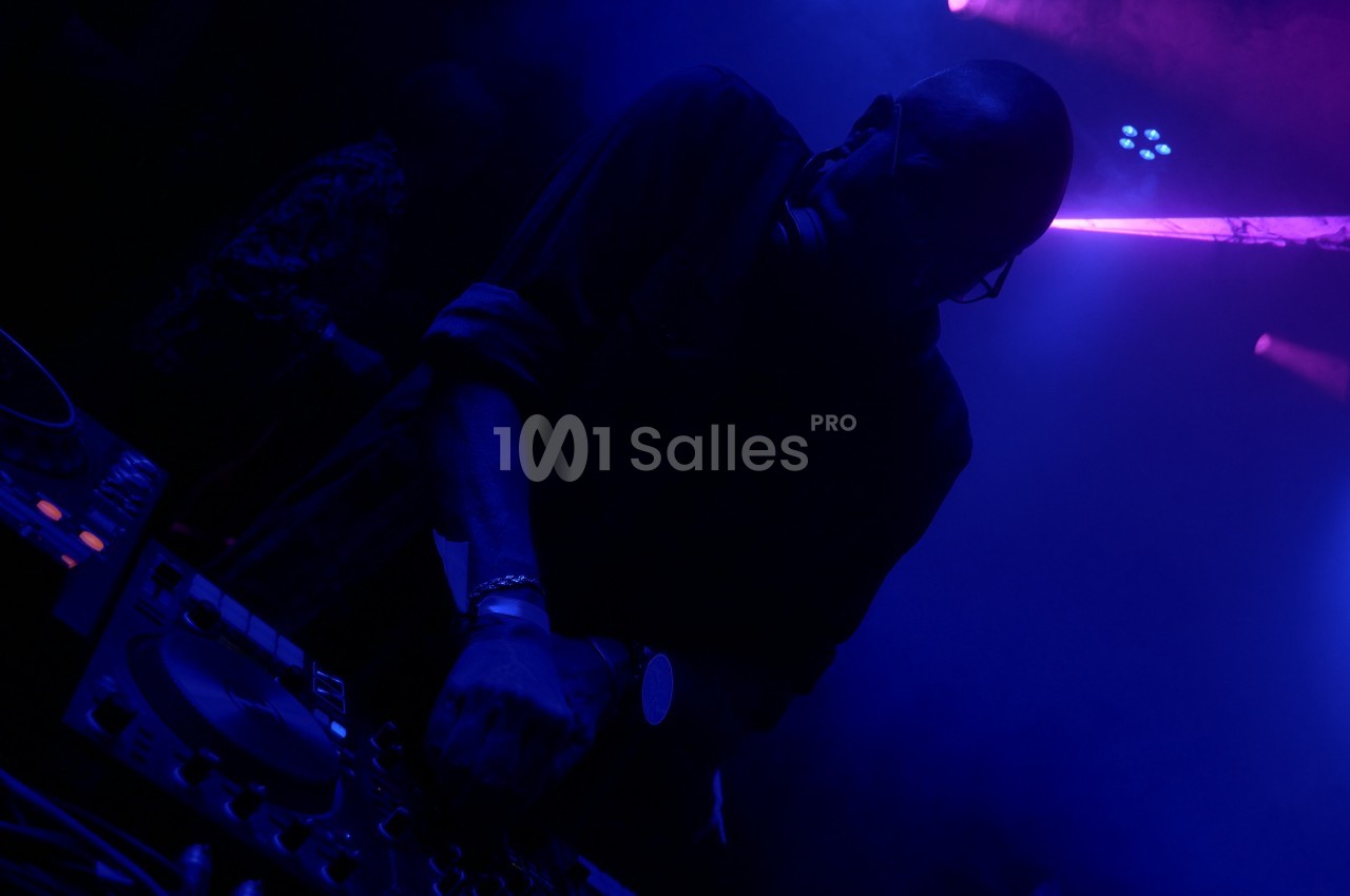 Un DJ mixant de la musique dans une ambiance sombre avec des lumières bleues et violettes.