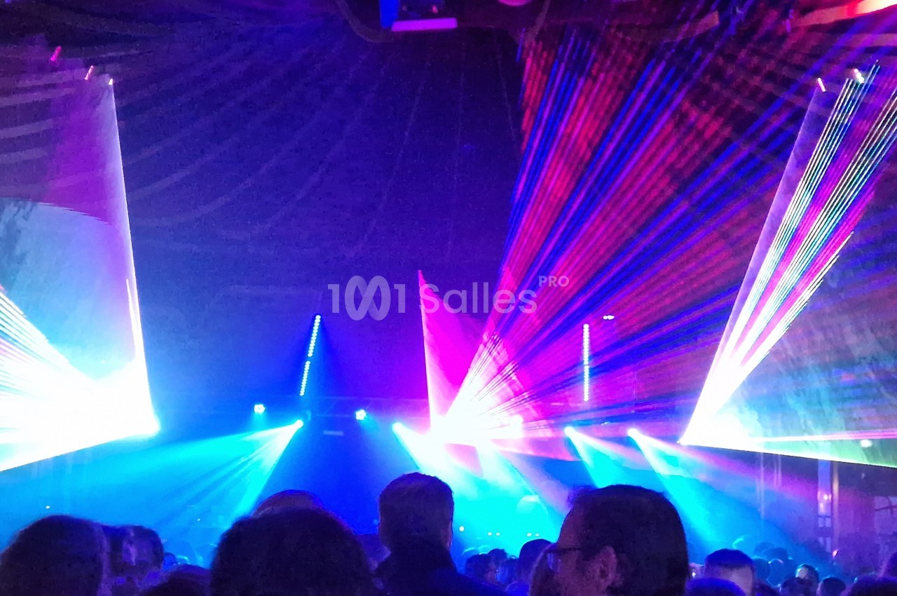 Foule dans une salle sombre illuminée par des faisceaux de lumière colorés et des effets laser.