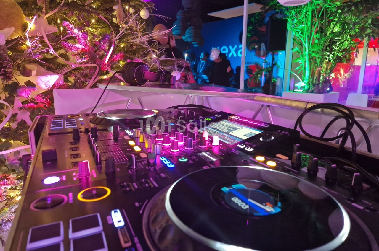 Table de mixage éclairée dans un environnement festif avec des lumières colorées et des plantes en arrière-plan.