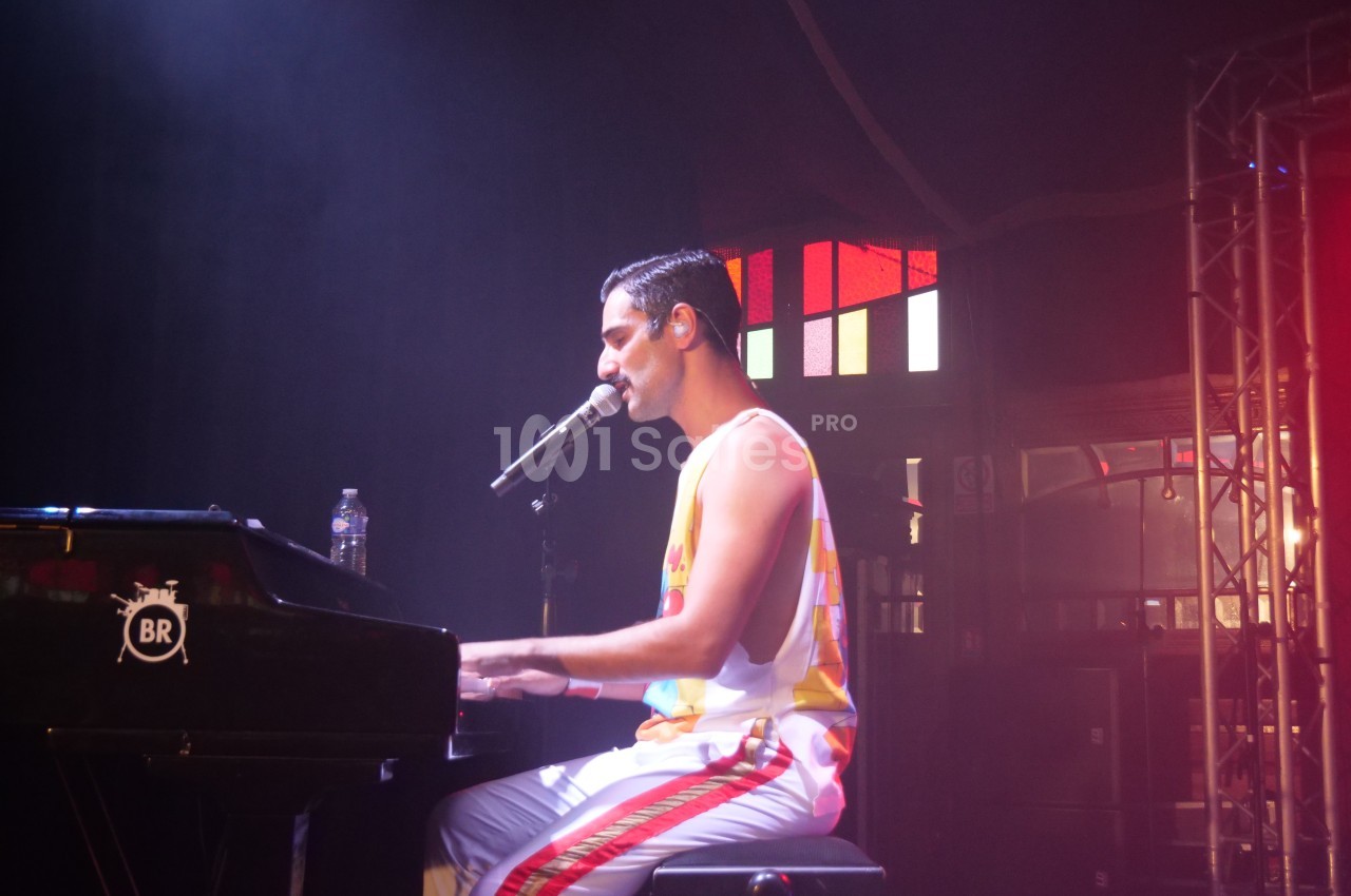 Un musicien joue du piano et chante sur scène, éclairé par des lumières colorées dans une ambiance de concert.