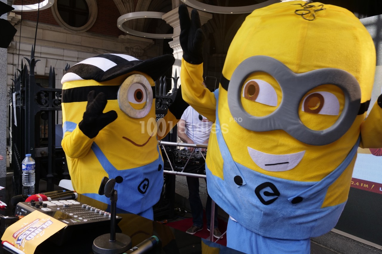 Deux mascottes jaunes déguisées en personnages de dessin animé interagissent joyeusement devant une table de mixage.