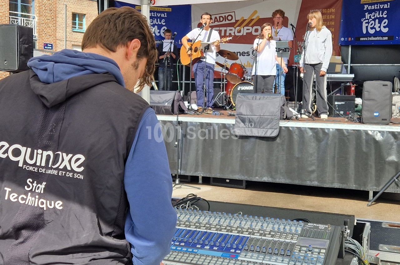 Un technicien ajuste une console de mixage lors d'un concert en plein air avec un groupe jouant sur scène.