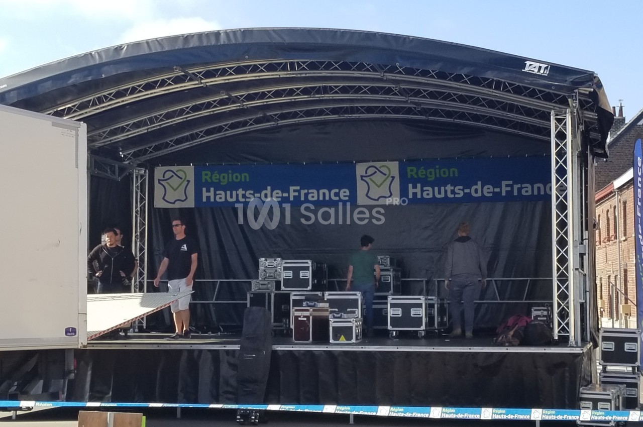Scène extérieure en cours de montage avec des techniciens et du matériel, sous une bannière ’Région Hauts-de-France’.