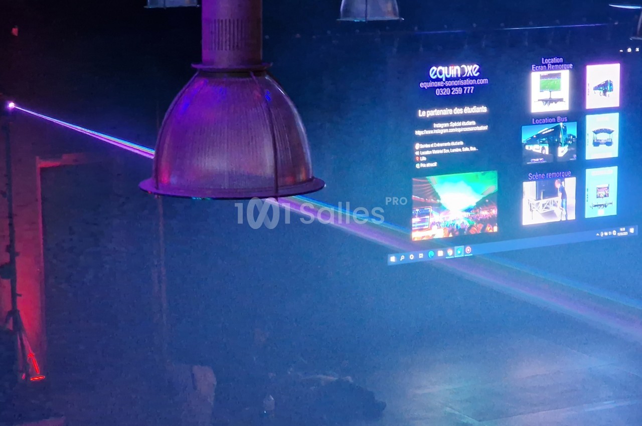 Faisceau lumineux coloré traversant une salle sombre avec un écran affichant des informations en arrière-plan.