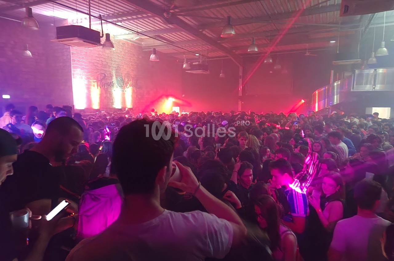 Foule dense dans une salle de concert avec éclairages colorés et ambiance festive.