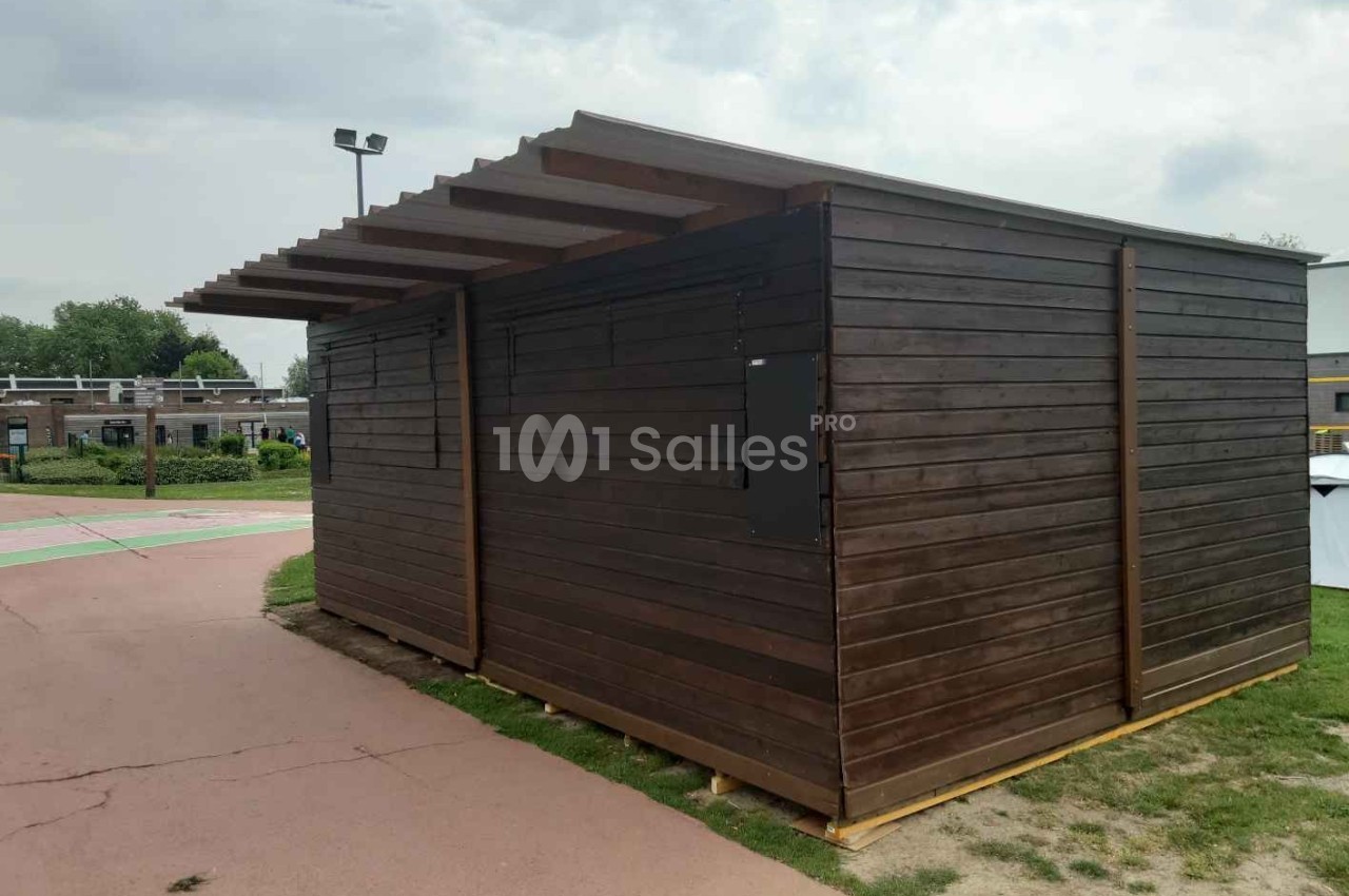 Abri en bois sombre avec toit incliné, situé sur un chemin pavé dans un espace extérieur dégagé.