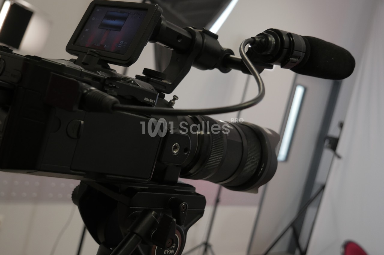 Caméra professionnelle avec micro montée sur trépied dans un studio avec éclairage et fond blanc.