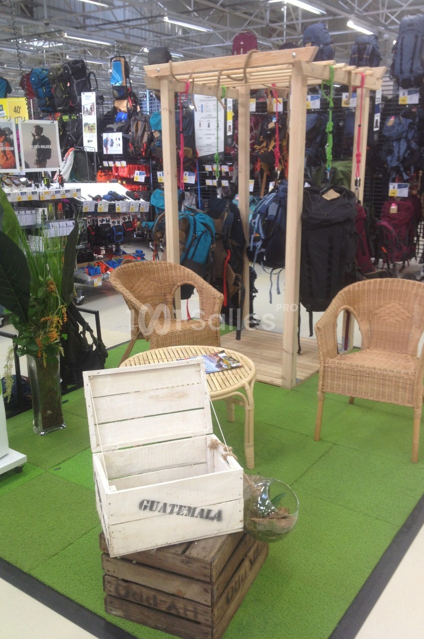 Espace d'exposition en magasin avec mobilier en rotin, plantes décoratives et présentoirs de sacs à dos en arrière-plan.