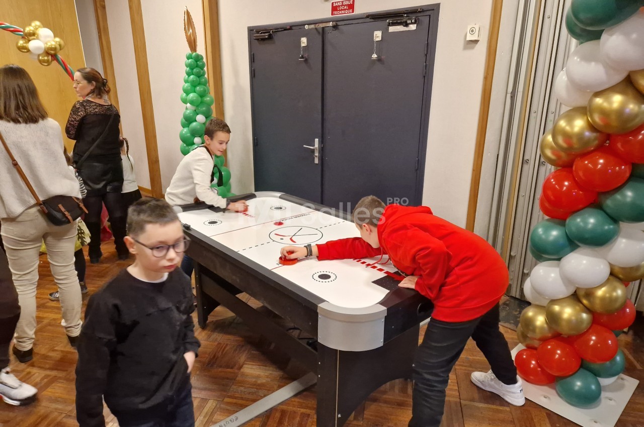 Deux enfants jouent à un jeu de hockey sur table dans une salle décorée de ballons colorés.
