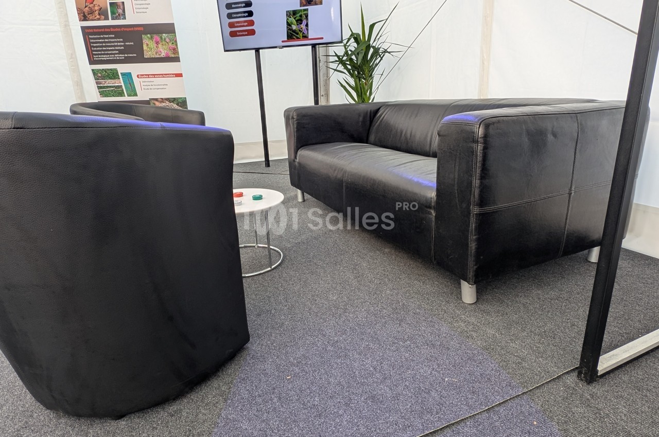 Deux fauteuils et un canapé en cuir noir disposés autour d'une petite table dans un espace intérieur avec moquette.