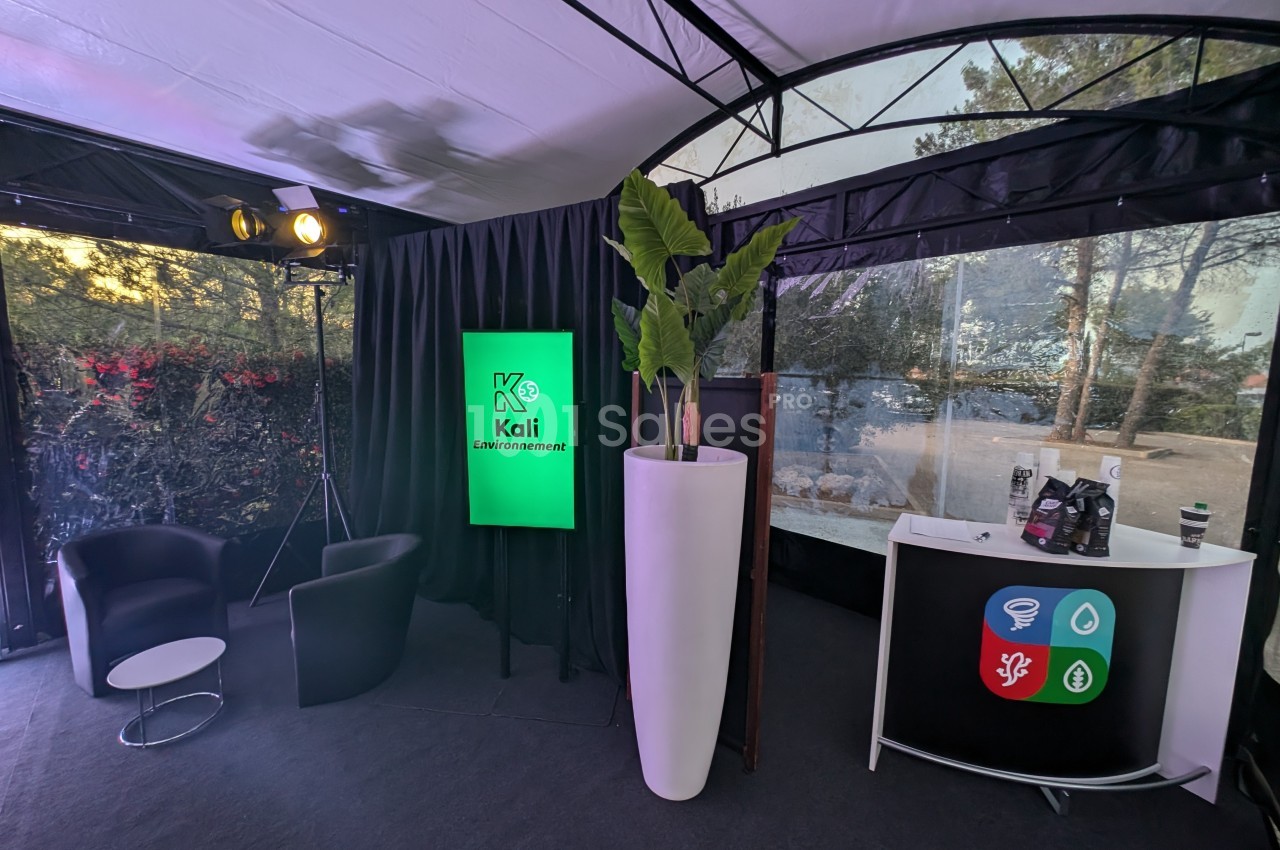Espace intérieur avec fauteuils, écran affichant ’Kali Environnement’, plante décorative et comptoir d'accueil.