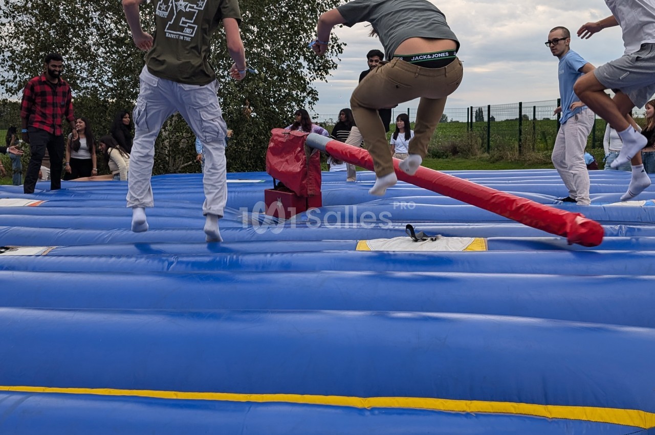 Des personnes sautent sur une structure gonflable bleue lors d'une activité en plein air, avec des obstacles rouges.