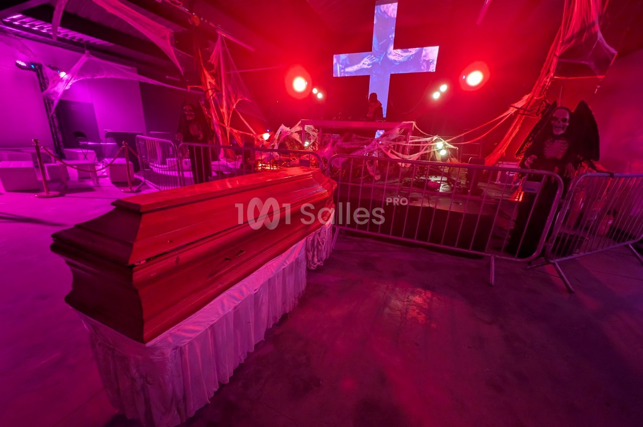 Cercueil en bois dans une ambiance sombre et lumineuse, décorée de toiles d'araignée et éclairée par des lumières rouges.
