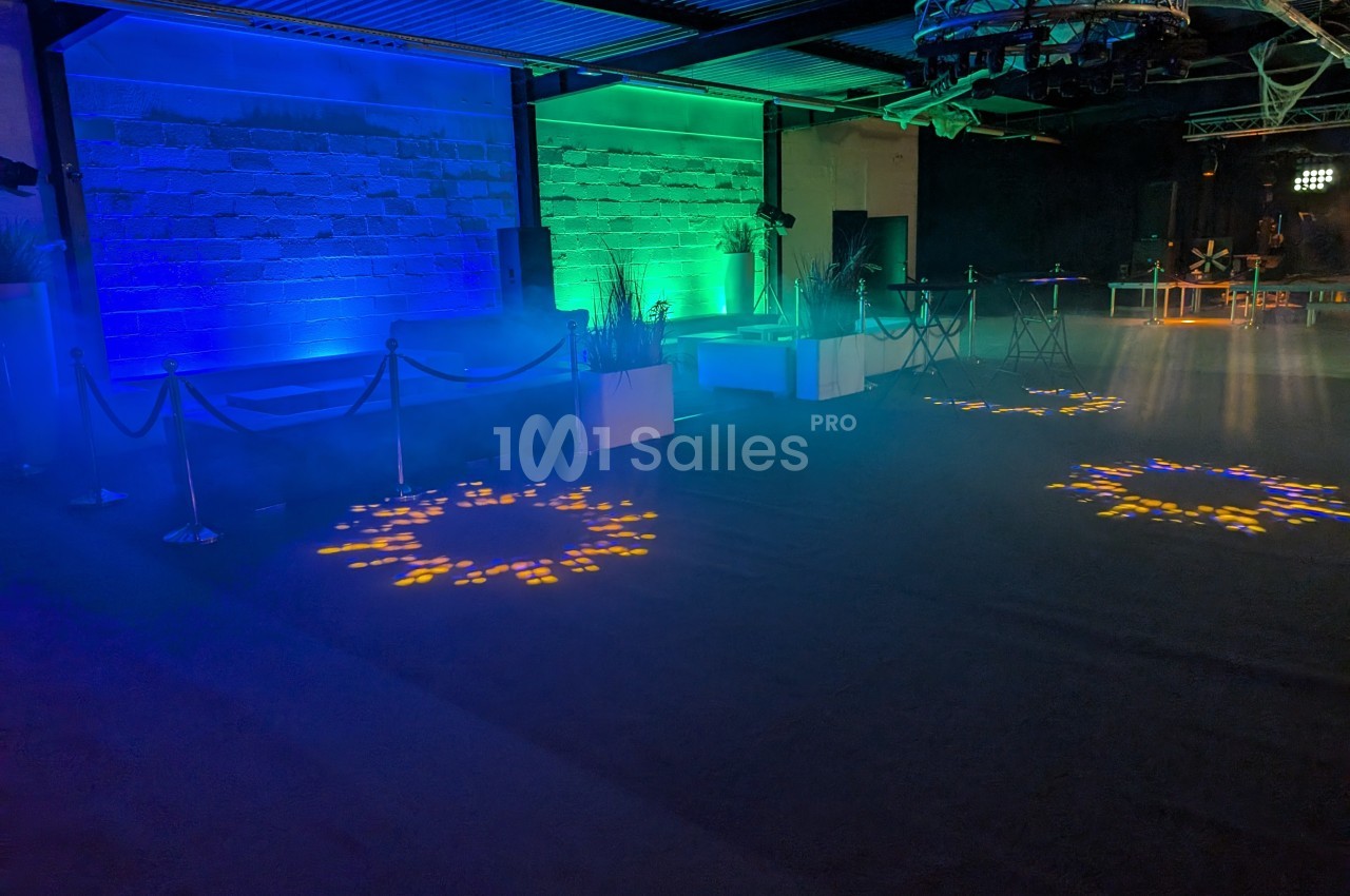 Salle sombre avec éclairage coloré bleu et vert, motifs lumineux au sol, mobilier moderne et espace dégagé.