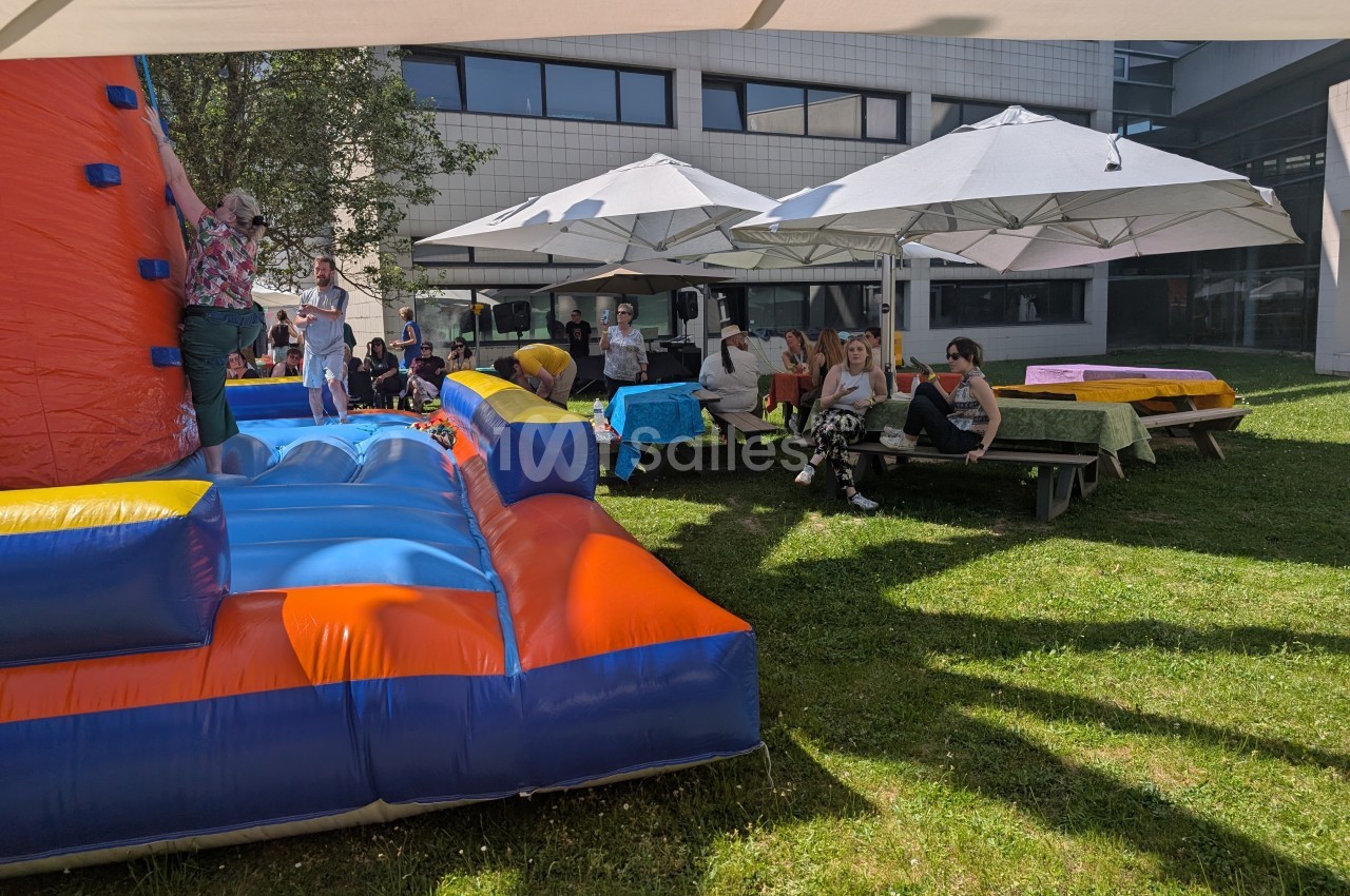 Personnes assises et discutant sous des parasols dans un espace extérieur, avec une structure gonflable colorée au premier…