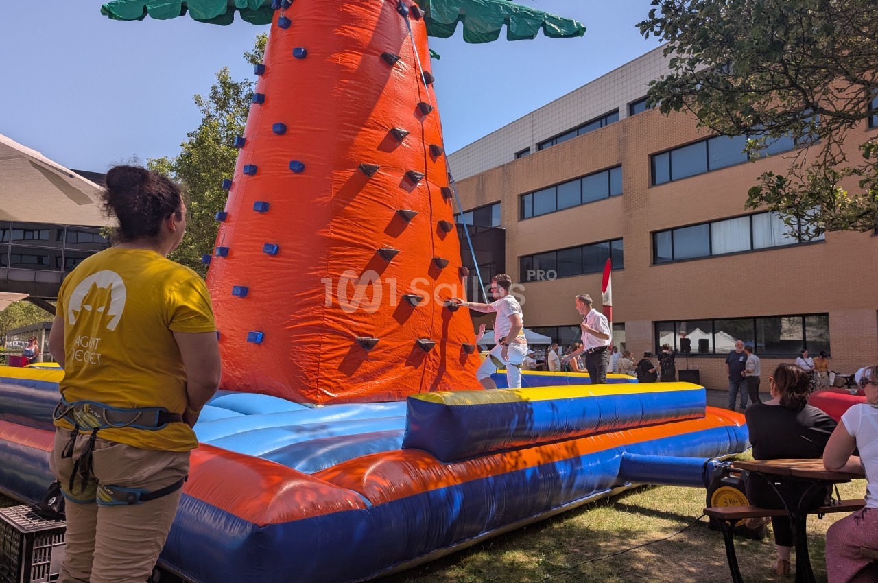 Une structure gonflable en forme de carotte utilisée pour une activité d'escalade en plein air, encadrée par des animateurs.