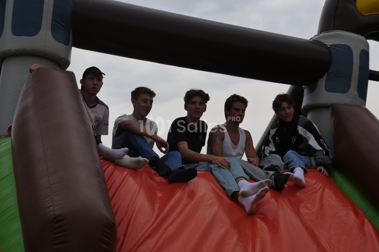 Cinq jeunes assis en haut d'un toboggan gonflable coloré sous un ciel nuageux.