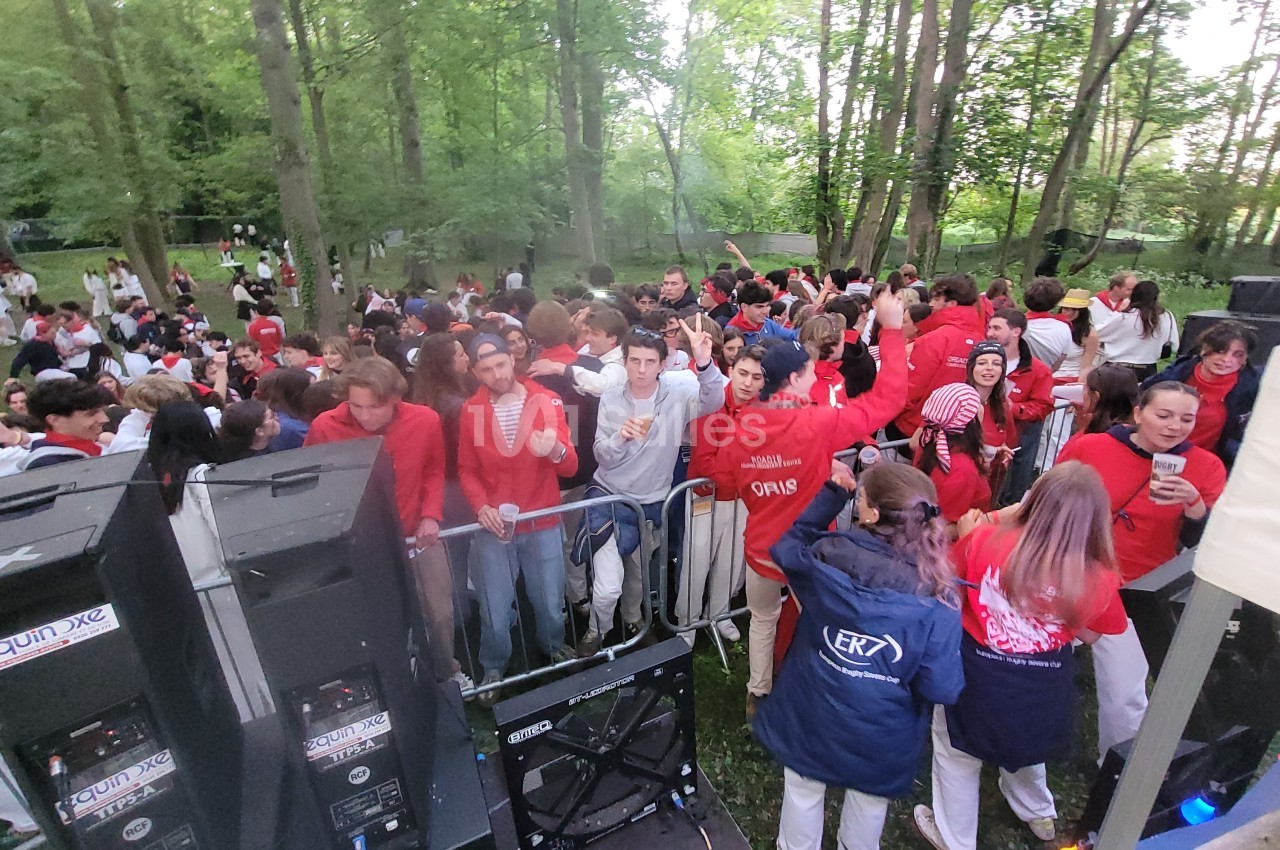 Groupe de personnes en tenue rouge et blanche dans une fête en plein air, entourées d'arbres et de matériel audio.