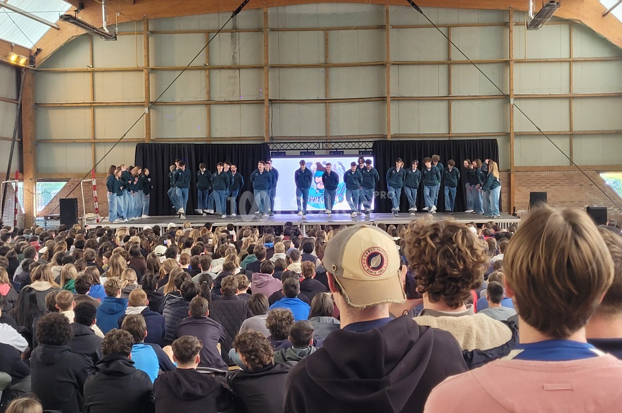Un groupe de danseurs sur scène devant un large public dans une salle avec une structure en bois.
