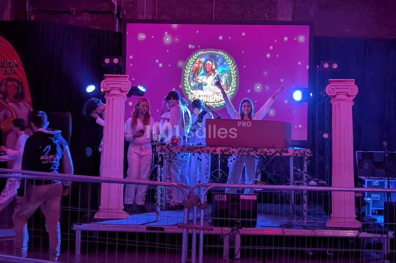 Des personnes en tenue blanche animent une soirée sur une scène décorée de colonnes et d'un écran lumineux.