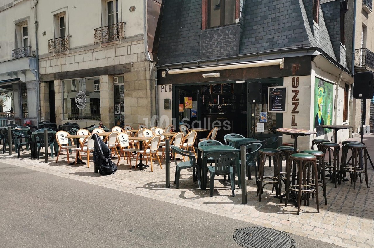 Terrasse d'un pub avec des tables et chaises en plein air, située dans une rue pavée devant un bâtiment ancien.