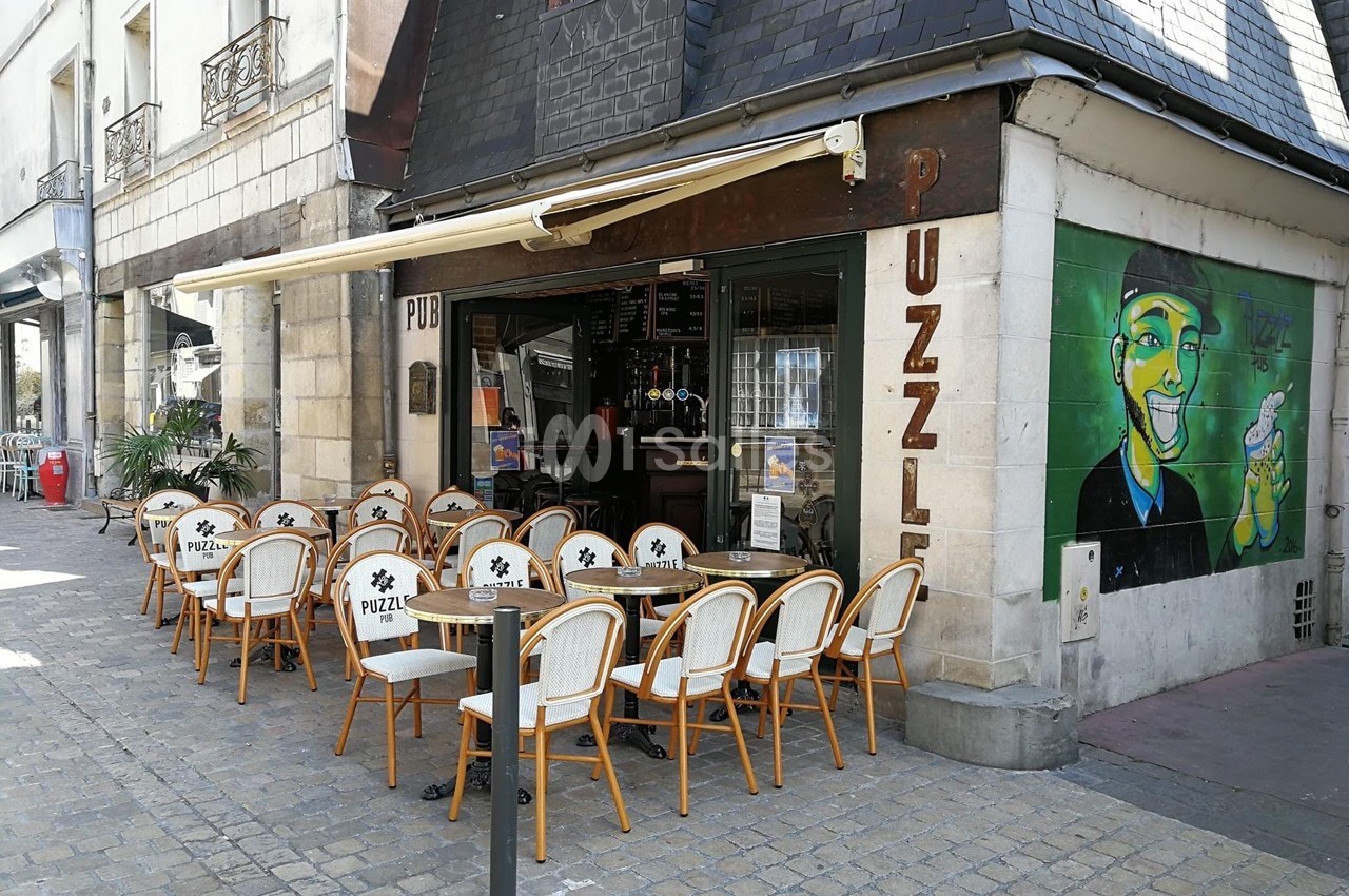 Terrasse d'un café avec des chaises en rotin disposées devant une façade ornée d'une fresque colorée.