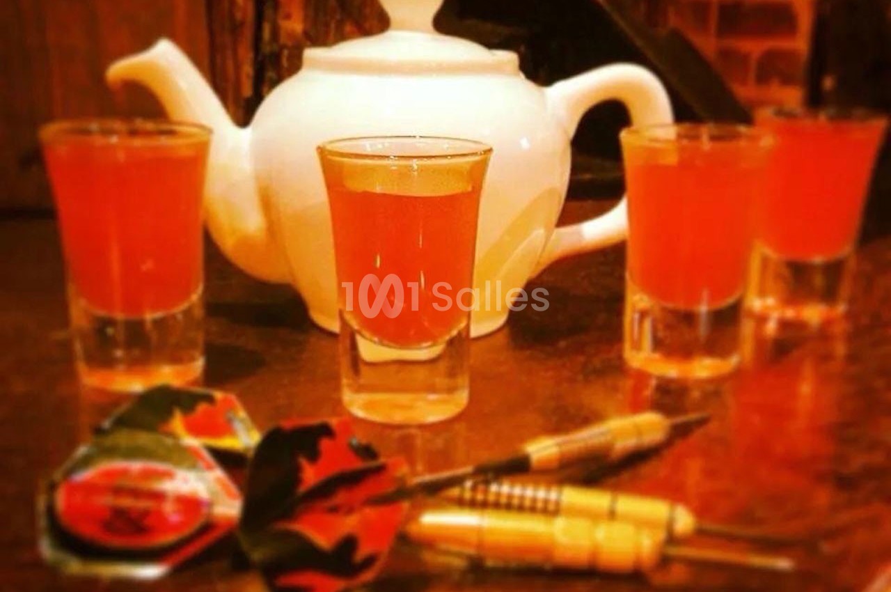 Théière blanche entourée de quatre verres de liquide orange, avec des fléchettes posées au premier plan.