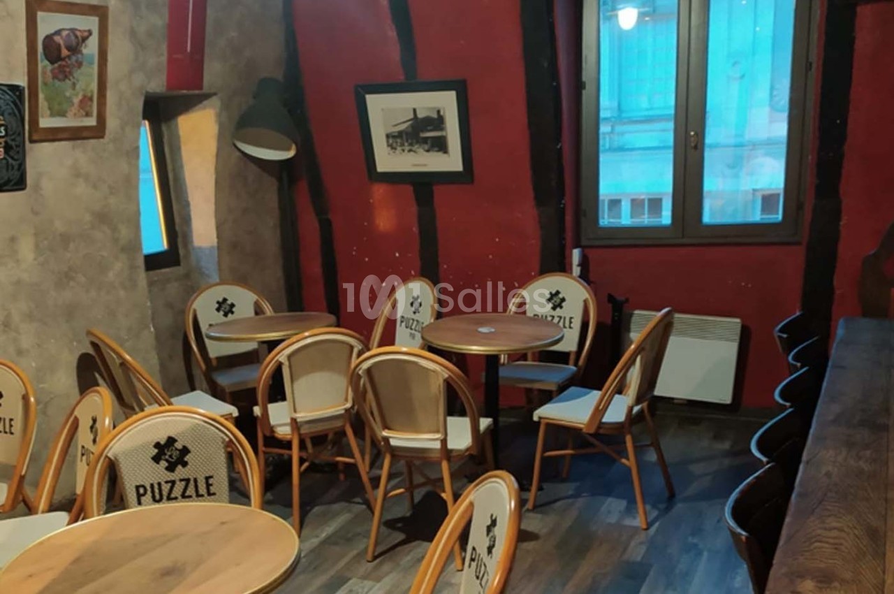 Salle de café avec des tables rondes, des chaises en bois clair et un mur rouge décoré de cadres.