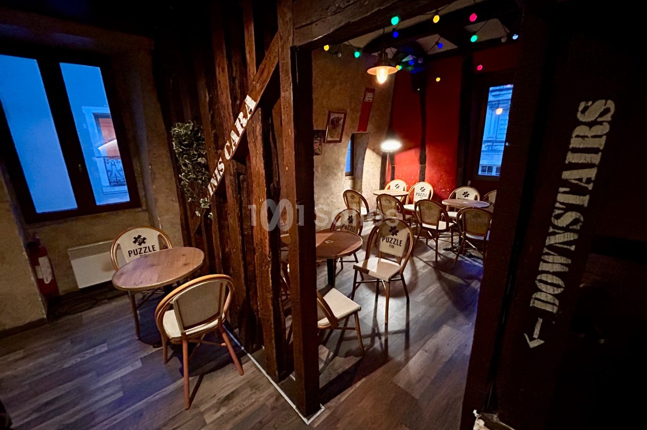 Salle intérieure chaleureuse avec tables, chaises en bois et guirlandes lumineuses colorées, ambiance conviviale.