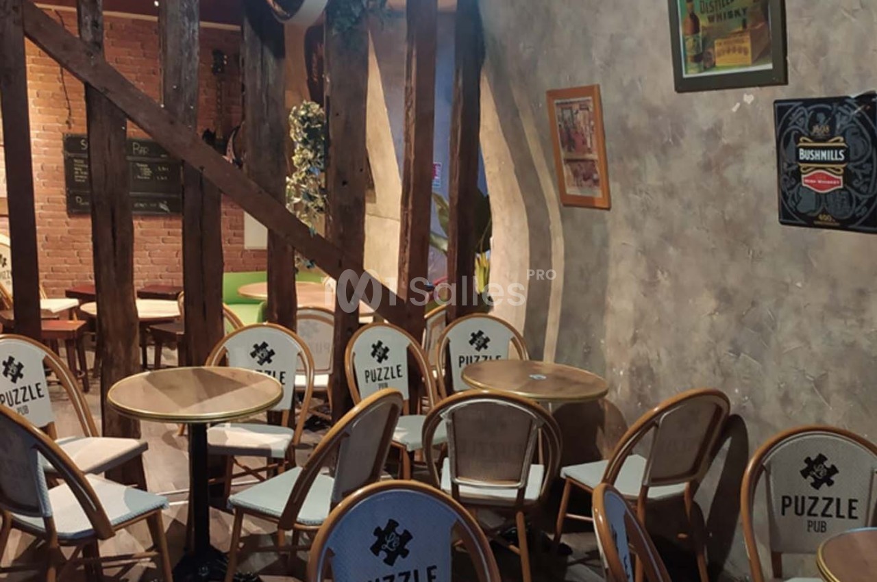 Chaises et tables en bois dans un espace intérieur avec murs texturés, poutres apparentes et décorations murales.