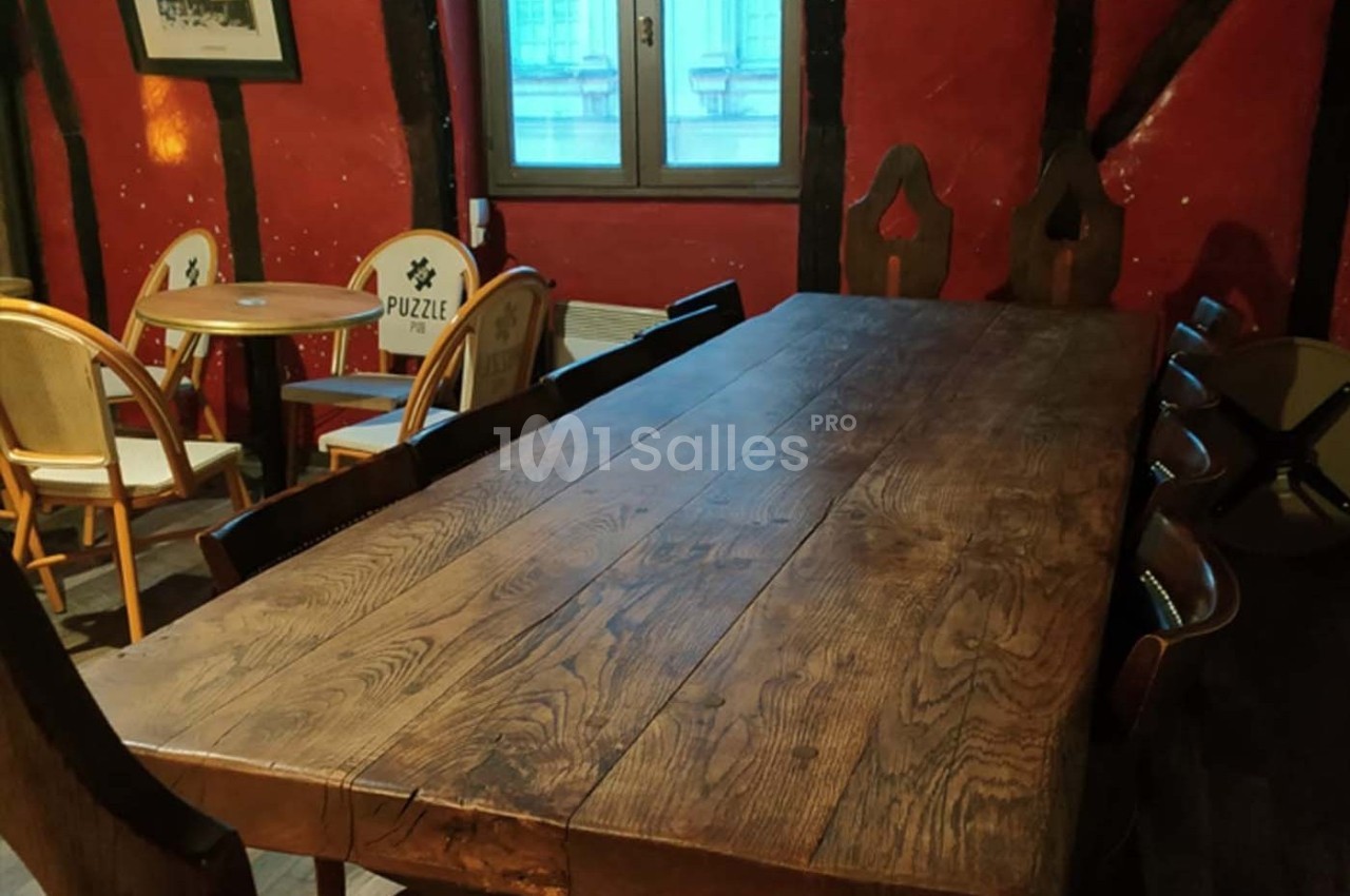 Grande table en bois massif entourée de chaises dans une pièce aux murs rouges avec poutres apparentes.