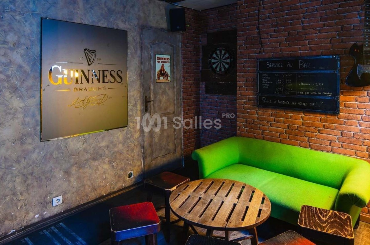 Espace intérieur avec canapé vert, table basse en bois, mur en briques, tableau noir et décoration de bar.