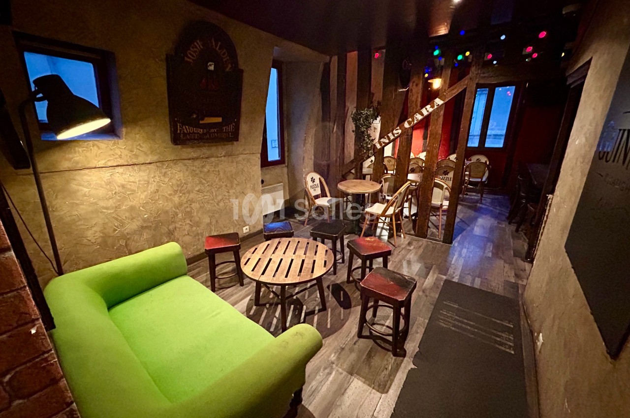 Salle chaleureuse avec canapé vert, tables en bois, chaises et éclairage tamisé, ambiance conviviale.