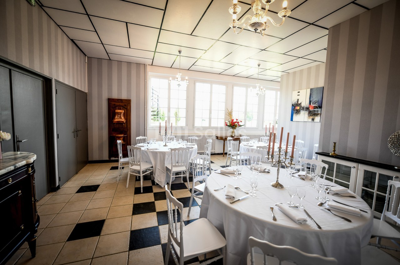 Salle de réception lumineuse avec tables rondes dressées, chaises blanches et décoration élégante.