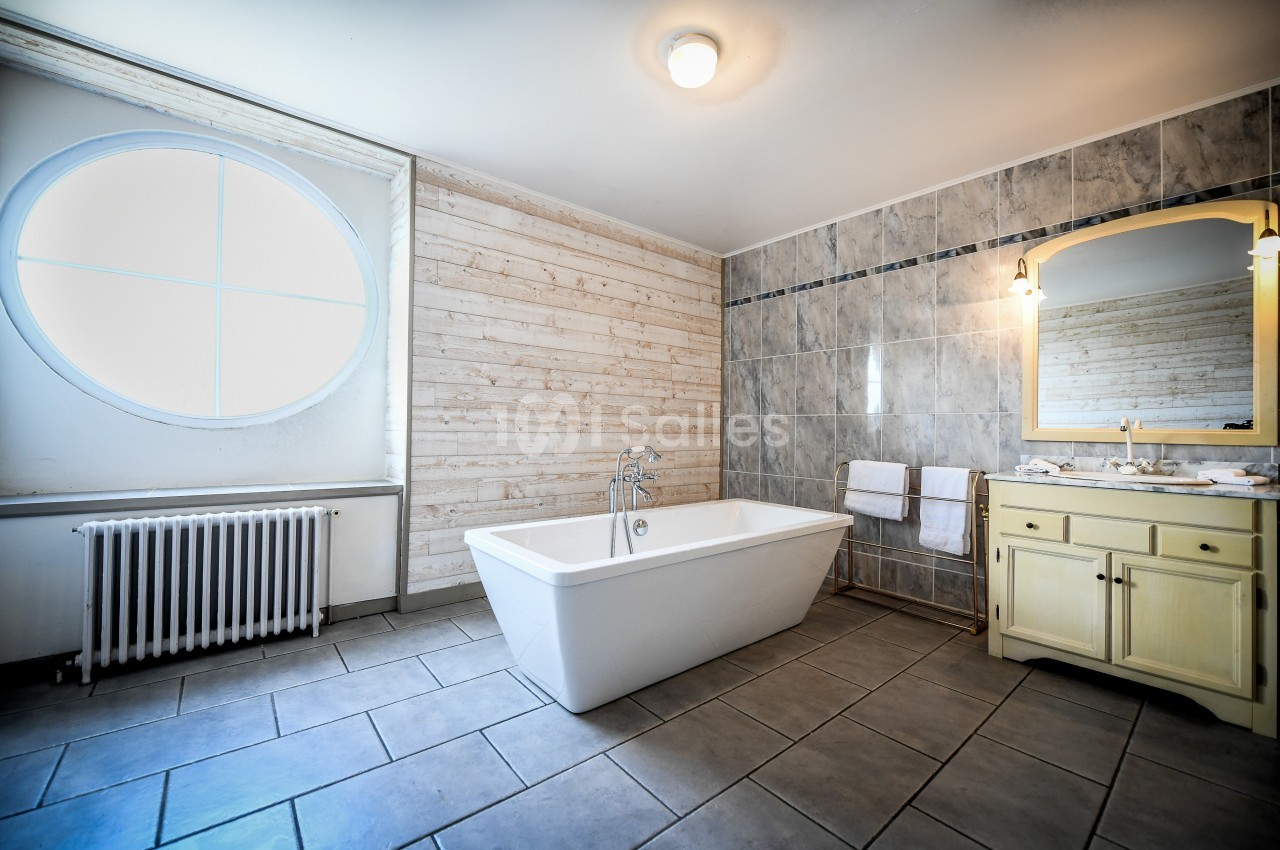 Salle de bain lumineuse avec baignoire blanche, mur en bois clair, carrelage gris et meuble lavabo jaune.