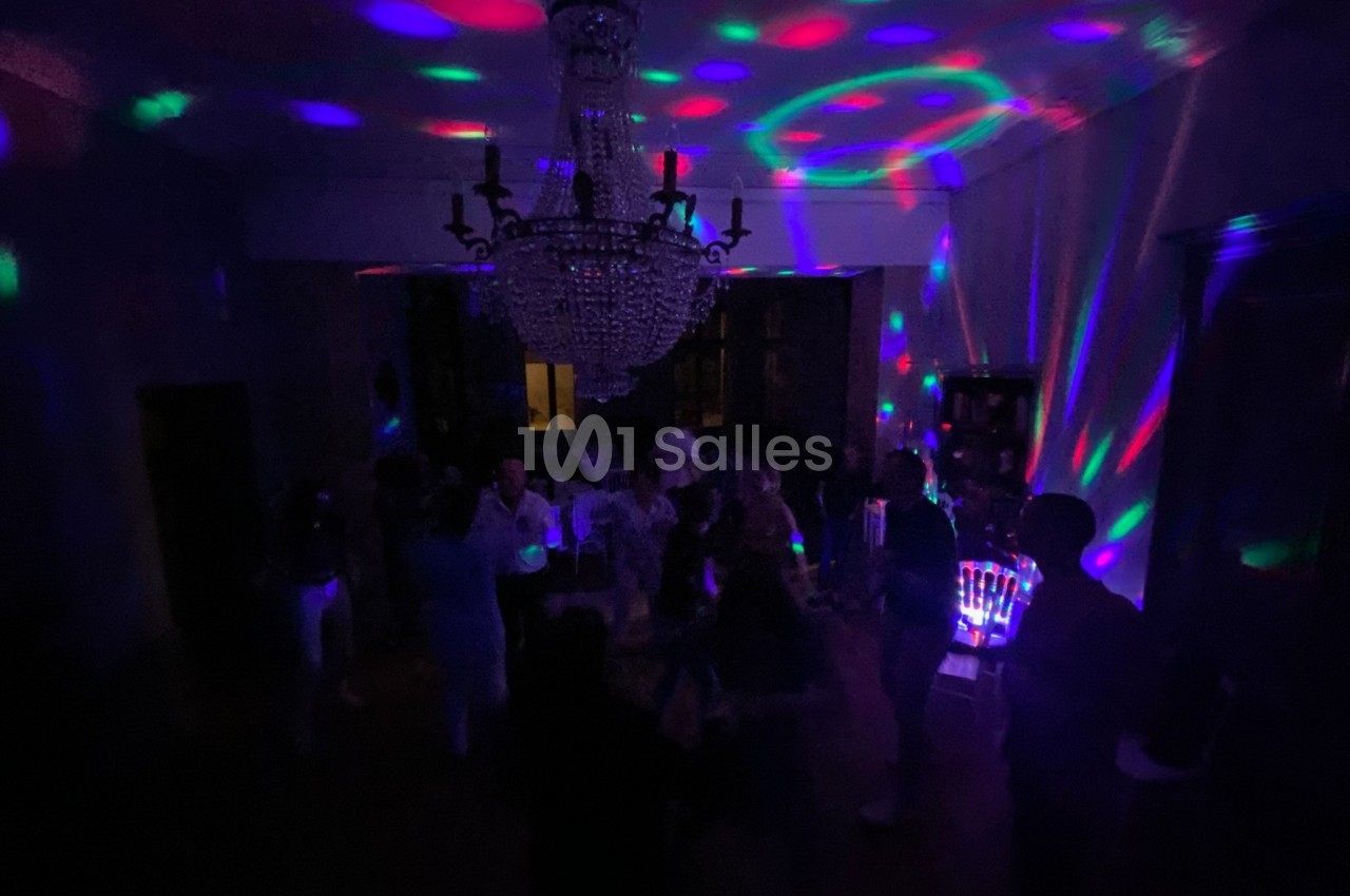 Personnes dansant dans une pièce sombre éclairée par des lumières colorées et un grand lustre central.