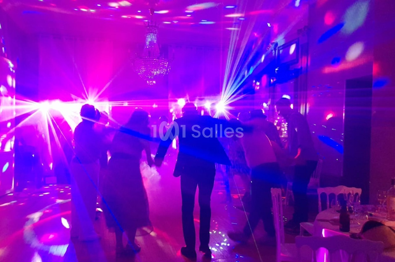 Des personnes dansent sous des lumières colorées dans une salle éclairée par un lustre.