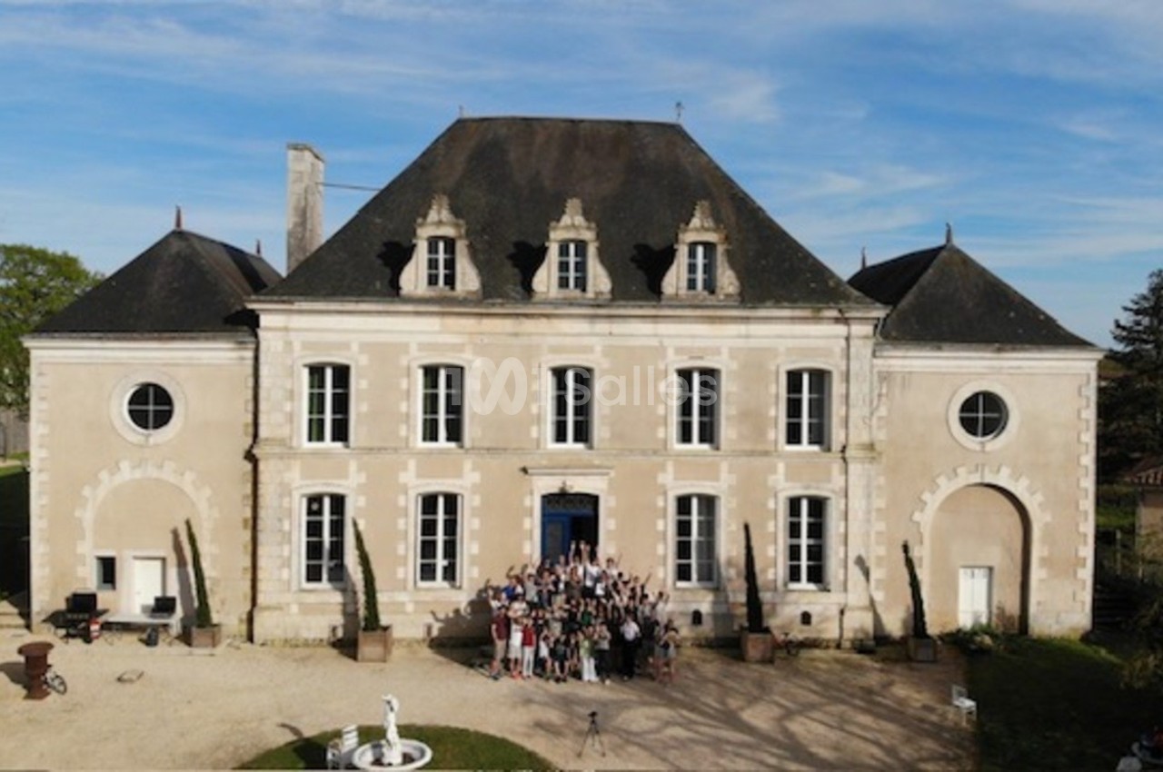 Façade d'un château ancien en pierre avec un groupe de personnes rassemblées devant l'entrée principale.