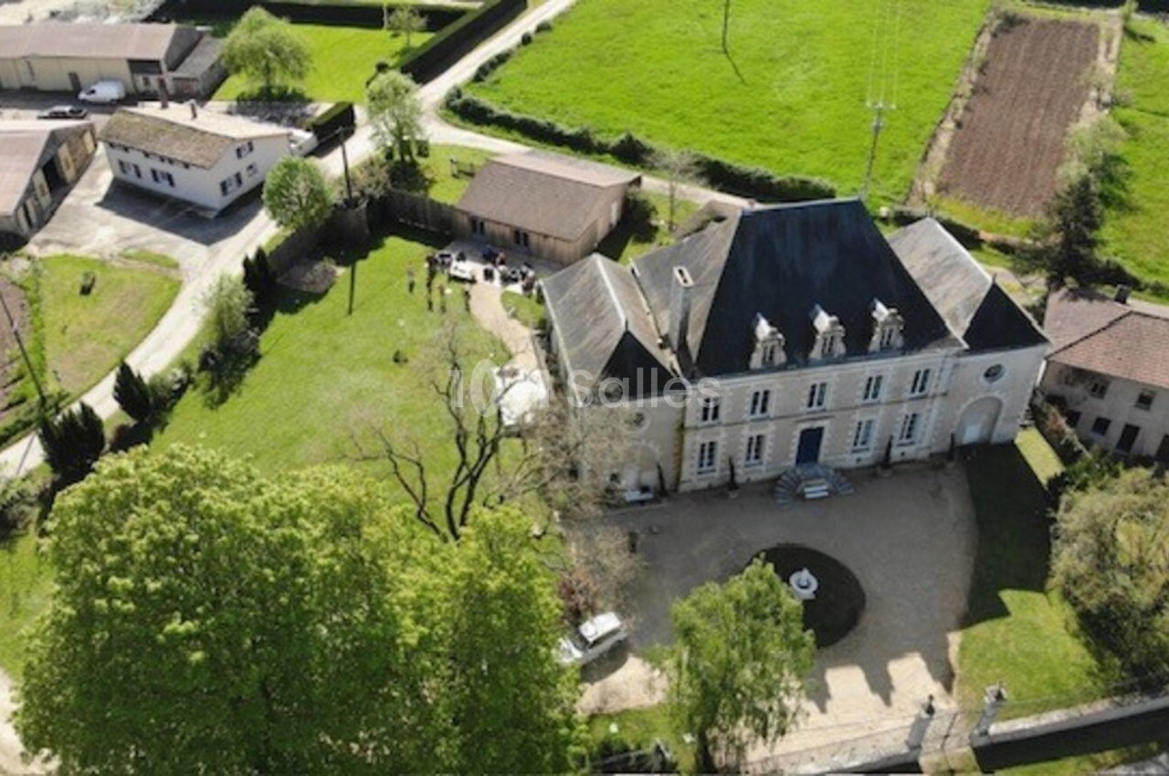 Vue aérienne d'un manoir entouré de jardins, avec des bâtiments annexes et des champs à proximité.